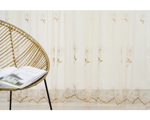 Perdea decorativă cu model floral lângă un scaun de ratan și o carte.