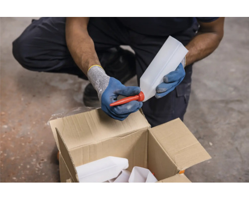 O persoană atașează un gât de scurgere roșu unei sticle goale de plastic deasupra unei cutii de carton.