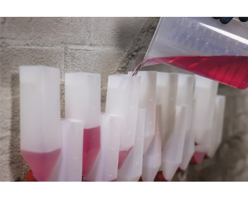 Umplerea unui rând de recipiente transparente cu lichid roșu dintr-un pahar gradat