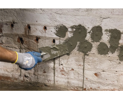 O persoană aplică tencuială pe un perete de cărămidă cu găuri