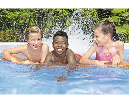 Trei copii zâmbesc într-o piscină pe o saltea pneumatică.