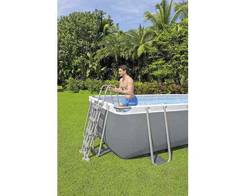 Bărbat care intră într-o piscină dreptunghiulară cu cadru de oțel într-o grădină folosind o scară