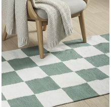 Scenă decorativă de podea cu covor cu model de tablă de șah sub un scaun cu pătură tricotată.