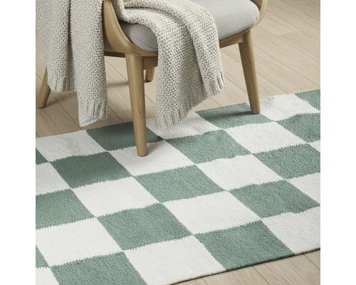 Scenă decorativă de podea cu covor cu model de tablă de șah sub un scaun cu pătură tricotată.