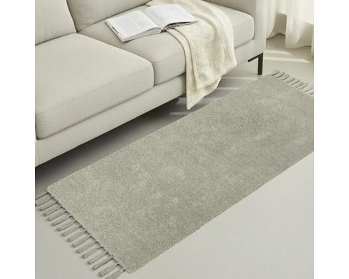 Covor gri cu franjuri lângă o canapea cu o carte