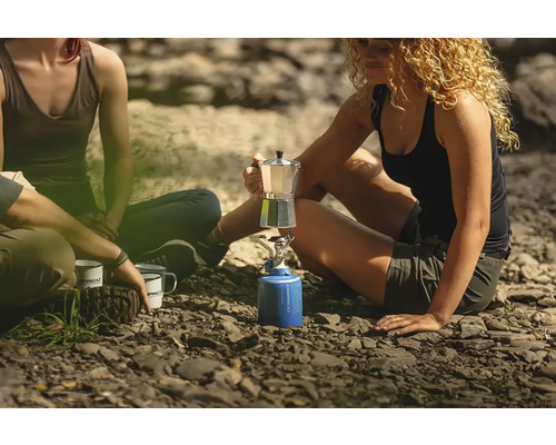 Scenă în aer liber cu aragaz de camping, ibric de cafea și persoane