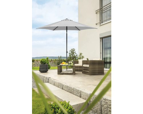 Scenă de grădină cu umbrelă de soare, fotolii din ratan și masă pe o terasă