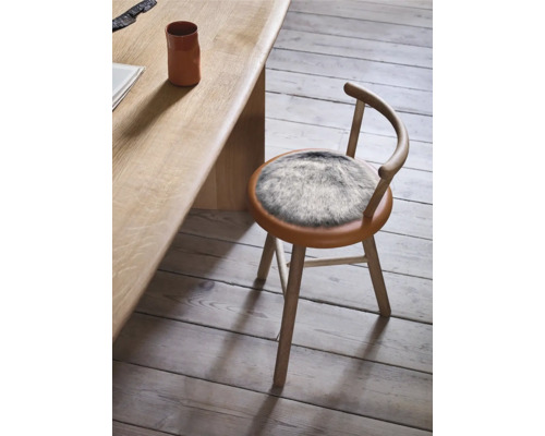 Scaun din lemn cu șezut rotund și suport din blană lângă masă din lemn