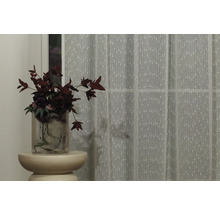 Cortină decorativă în fața ferestrei, completată de o vază cu flori pe o măsuță laterală.