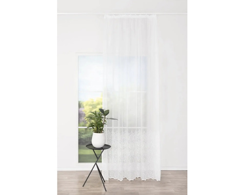 Cameră luminoasă cu draperie albă transparentă și plantă de apartament pe o măsuță laterală