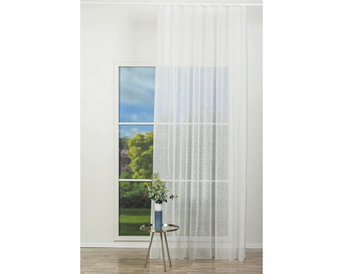 Fereastră cu perdea albă transparentă și o masă cu o vază cu flori