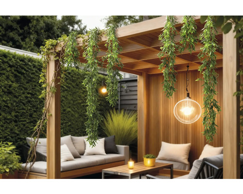 Pergolă din lemn decorată cu ghirlande artificiale de plante și o lampă suspendată într-un spațiu exterior luminos.