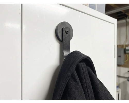 Cârlig magnetic negru pentru haine pe o suprafață albă cu o jachetă agățată