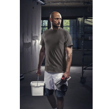 Muncitor cu tricou, pantaloni scurți, găleată și gletieră pe un șantier.