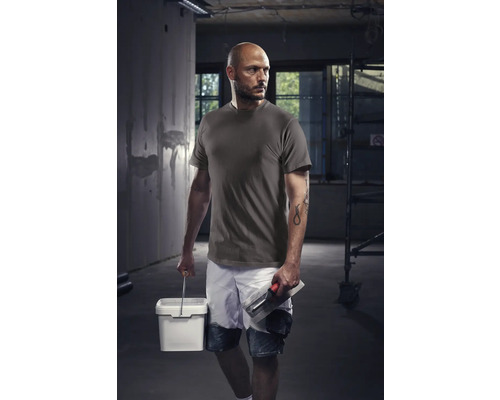 Muncitor cu tricou, pantaloni scurți, găleată și gletieră pe un șantier.