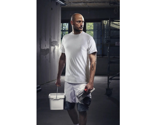 Meseriaș cu tricou, pantaloni scurți, găleată și gletieră pe un șantier