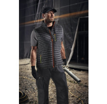 Bărbat purtând haine de lucru cu vestă, tricou, pantaloni și șapcă în fața unui șantier