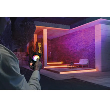 Casă cu iluminare colorată și persoană care controlează lumina cu un smartphone