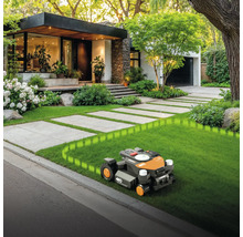 Robot de tuns iarba pe gazon în fața casei cu alee pavată
