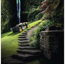 Scenă cu o mașină de tuns iarba robotizată pe un gazon verde lângă o scară de piatră