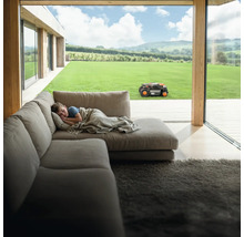 Băiat doarme pe canapea în timp ce robotul de tuns iarba lucrează în grădină