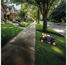 Un robot de tuns iarba tunde gazonul din fața unei case.