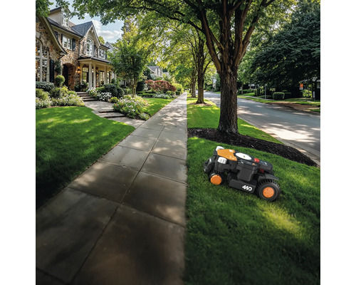 Un robot de tuns iarba tunde gazonul din fața unei case.