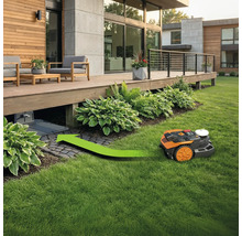 Robot de tuns iarba cu săgeată verde mergând spre stația de încărcare sub o terasă din lemn