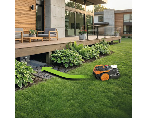 Robot de tuns iarba cu săgeată verde mergând spre stația de încărcare sub o terasă din lemn