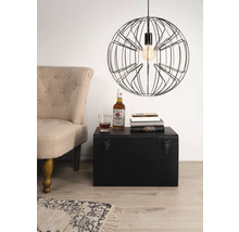 Scenă cu un fotoliu, un cufăr negru, cărți, o băutură și o lampă suspendată cu cadru metalic.