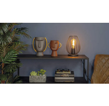 Scenă decorativă cu două vaze cu fețe, o lampă și o grămadă de cărți pe un raft.