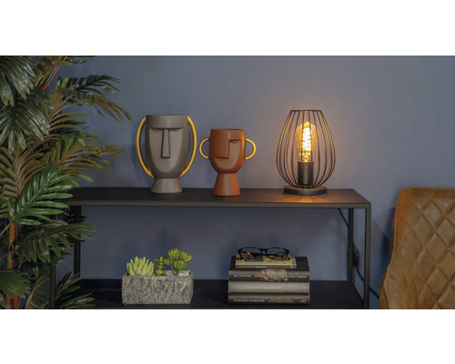 Scenă decorativă cu două vaze cu fețe, o lampă și o grămadă de cărți pe un raft.