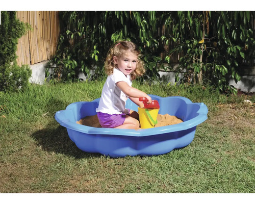 Fetiță se joacă într-o scoică de nisip albastră cu jucării de nisip în grădină.