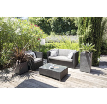 Scenă de grădină cu grup de ședere format din canapea, fotoliu și masă, precum și plante în jardiniere pe o terasă din lemn