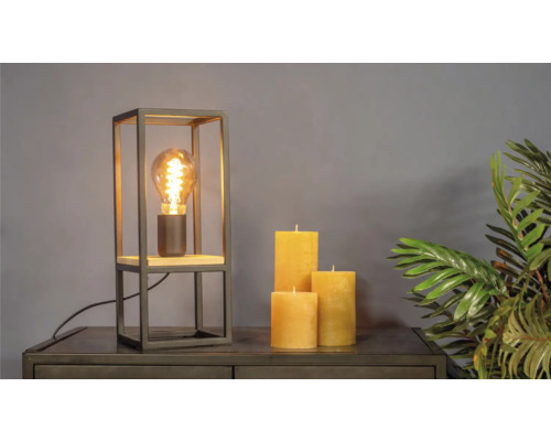 Lampă de masă decorativă cu bec Edison, lumânări și plantă de apartament pe o comodă.