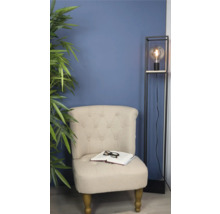 Fotoliu cu carte și ochelari lângă lampa de podea și plantă de apartament