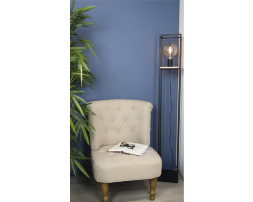 Fotoliu cu carte și ochelari lângă lampa de podea și plantă de apartament