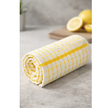 Prosop de bucătărie în carouri galben-alb, rulat pe un blat de bucătărie cu lămâi în fundal.