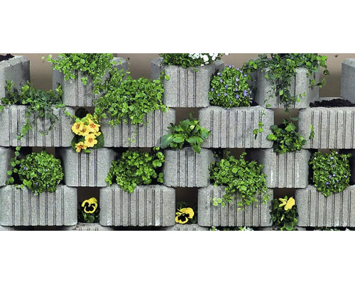 Zid din bolțari de beton gri pentru grădinărit, cu caneluri verticale, plantați cu diverse plante verzi și flori colorate.