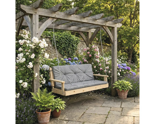 Scenă de grădină cu leagăn de lemn și pernă gri sub o pergolă, înconjurată de flori