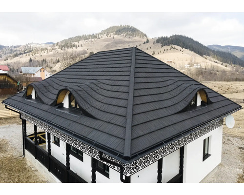 Casă cu acoperiș metalic și ferestre de mansardă în fața unui peisaj deluros