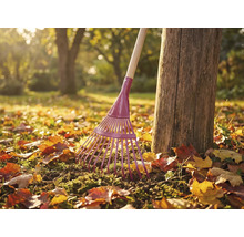 Greblă de grădină din metal cu mâner din lemn lângă trunchiul unui copac în grădină