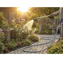 O persoană udă trandafiri cu un furtun de grădină pe un drum pavat.