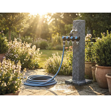 Scenă de grădină cu stâlp de apă, distribuitor multiplu și furtun de grădină pe terasă de piatră