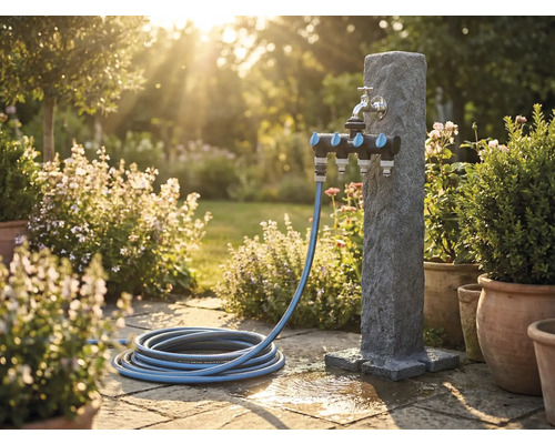 Scenă de grădină cu stâlp de apă, distribuitor multiplu și furtun de grădină pe terasă de piatră