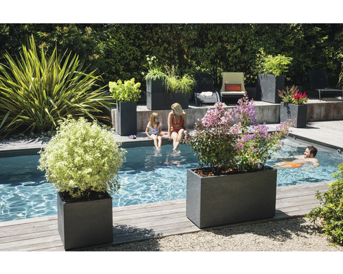 Scenă dintr-o grădină cu jardiniere dreptunghiulare din piatră, piscină, persoane care se bălăcesc și plante