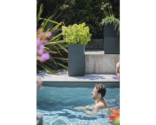 Scenă cu jardiniere gri pe o terasă de lemn lângă o piscină în care o persoană înoată