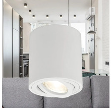 Lampă suspendată albă cu abajur cilindric deasupra unei canapele într-o sufragerie.