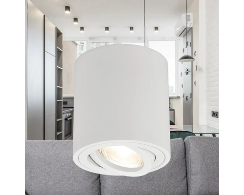 Lampă suspendată albă cu abajur cilindric deasupra unei canapele într-o sufragerie.