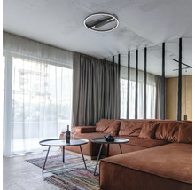 Sufragerie modernă cu plafonieră LED circulară, canapea mare maro și măsuțe de cafea rotunde în fața ferestrelor de la podea la tavan.